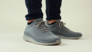 A person wearing dark pants and light gray Nexus Knit minimalist footwear by Xero Shoes with white soles, standing on a light surface. The shoes have laces and a textured pattern.